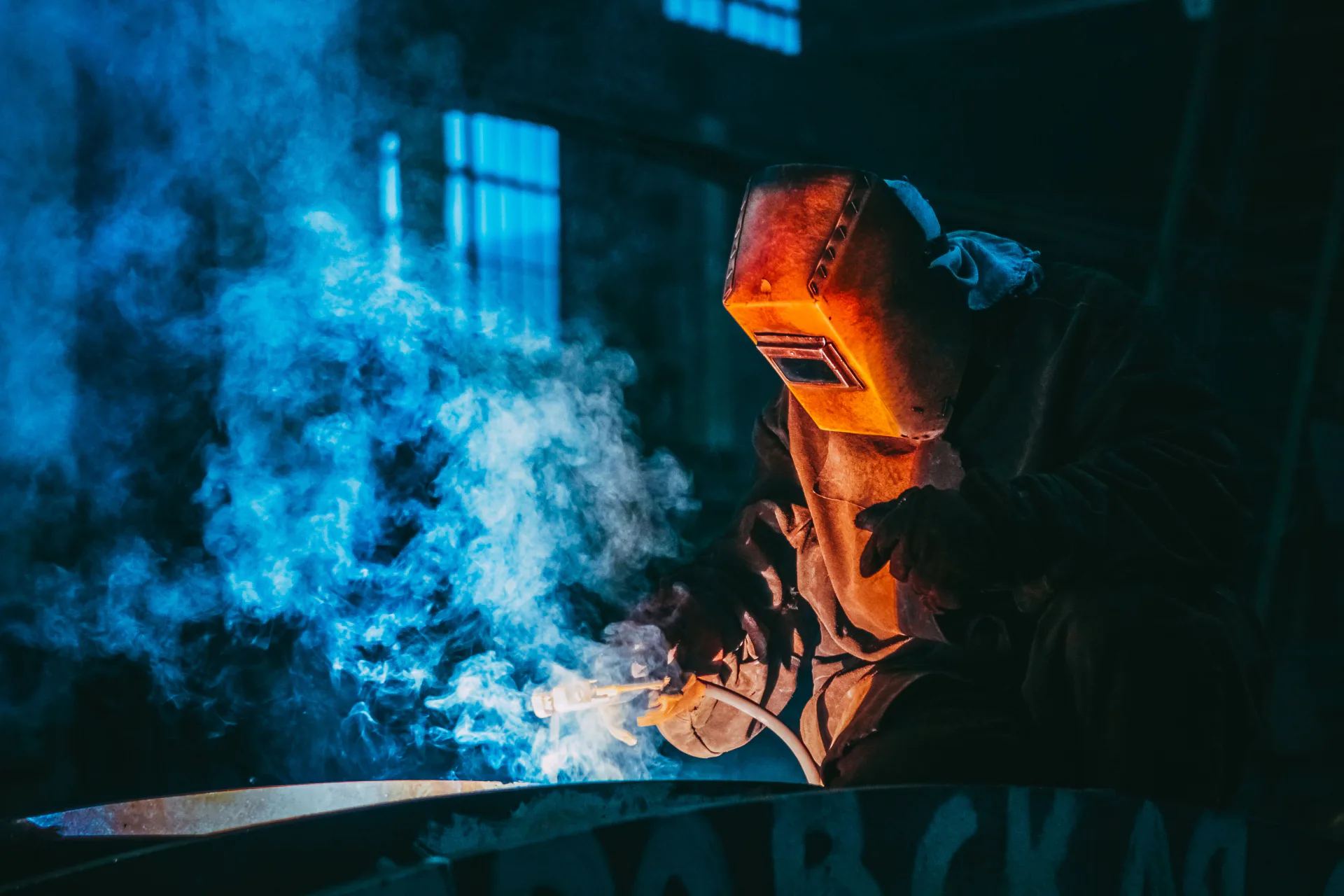 Welder surrounded by blue welding smoke while practicing an industrial welding process