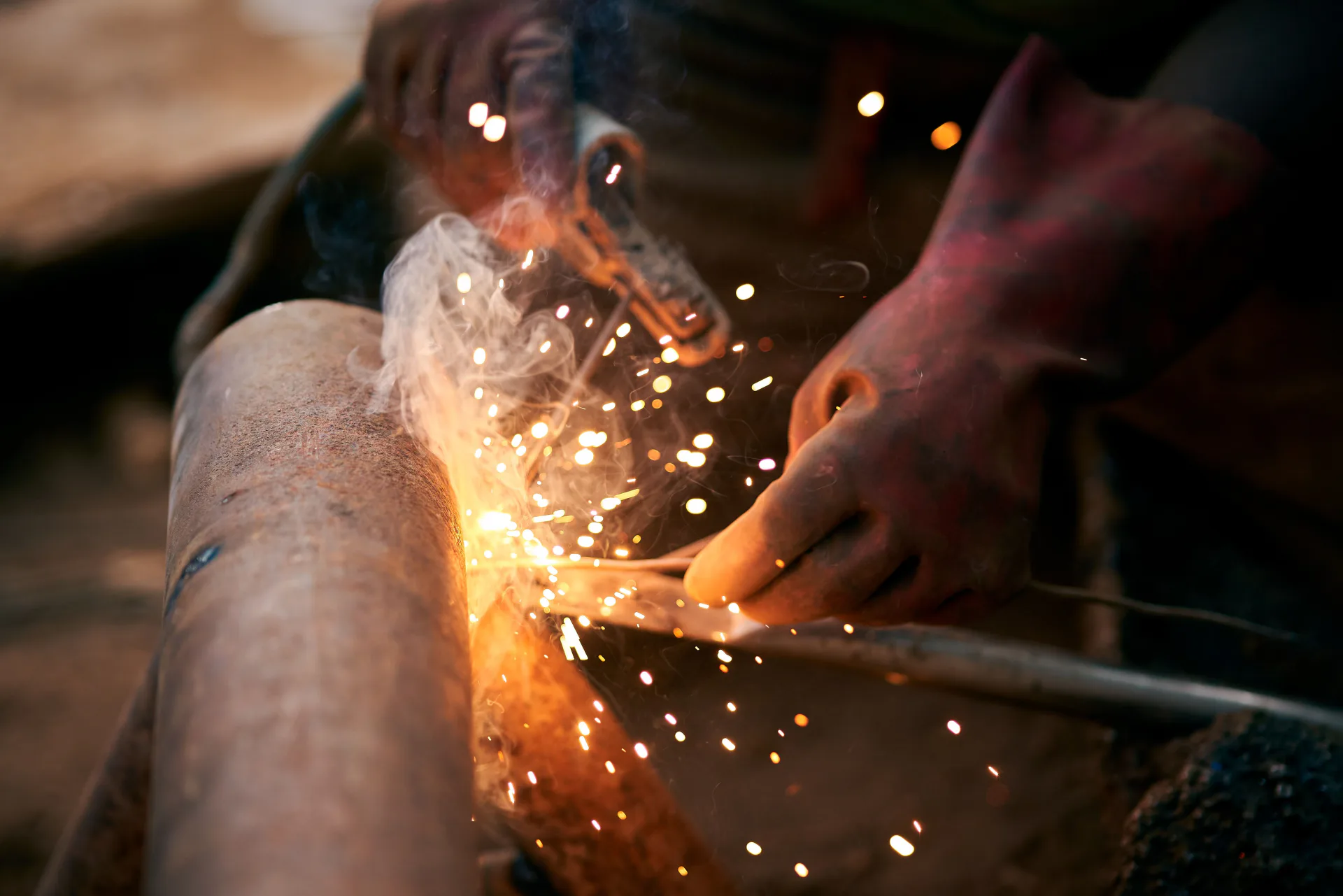 Close-up of a welder practicing controlled pipe welding with sparks and protective gloves